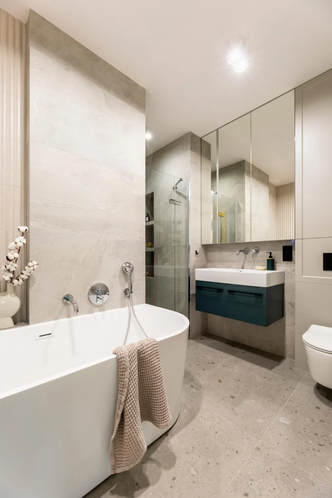 Badkamer met grote natuursteenlook wandtegels, vrijstaand bad en inloopdouche